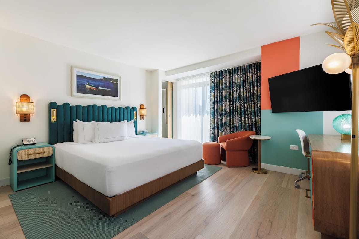 A modern hotel room with a large bed, a desk, a chair, a television, and a window with curtains.
