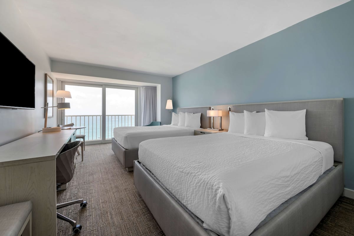 A hotel room with two beds, a desk, and a TV.
