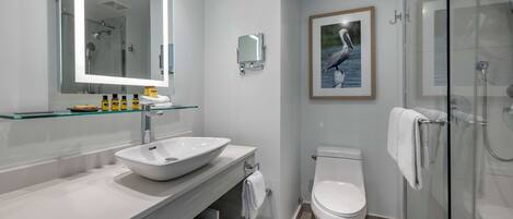 A modern bathroom with a large mirror, a white sink, a toilet, and a glass-enclosed shower.