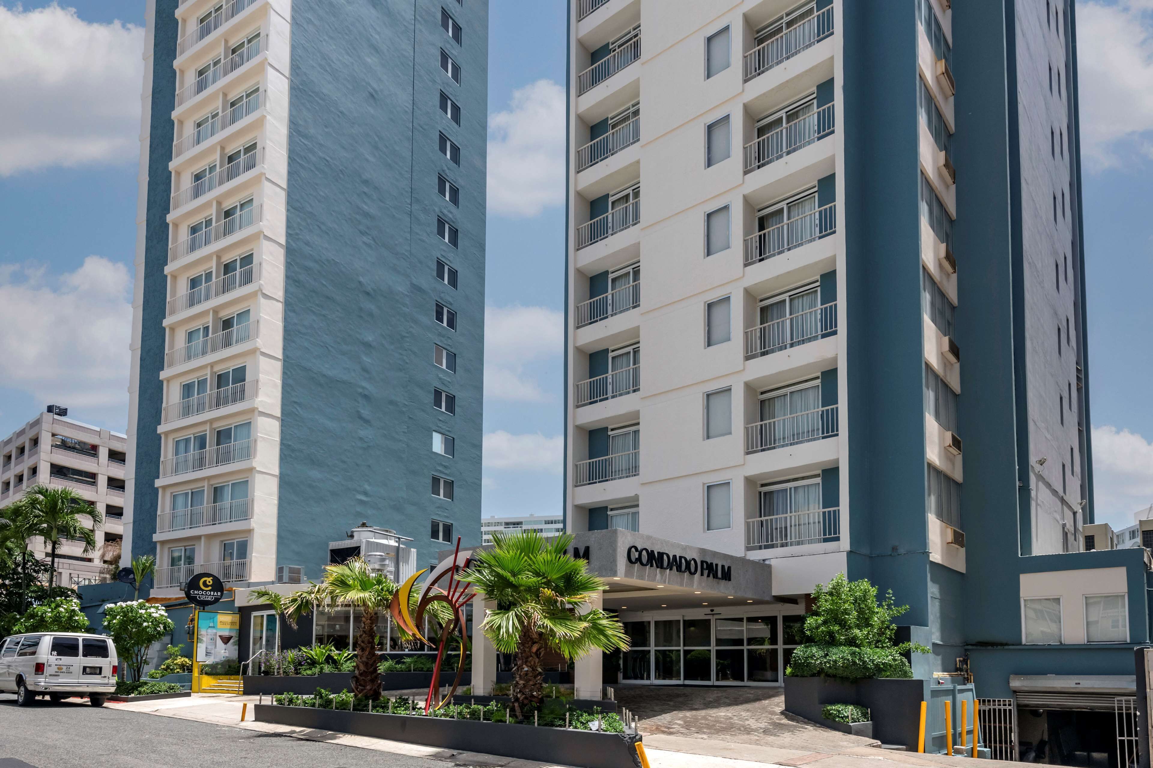Un hôtel moderne, reconnaissable à son grand panneau « CONDADO PALM », qui se distingue par son architecture à plusieurs étages, ses balcons et le ciel dégagé qui l’entoure.