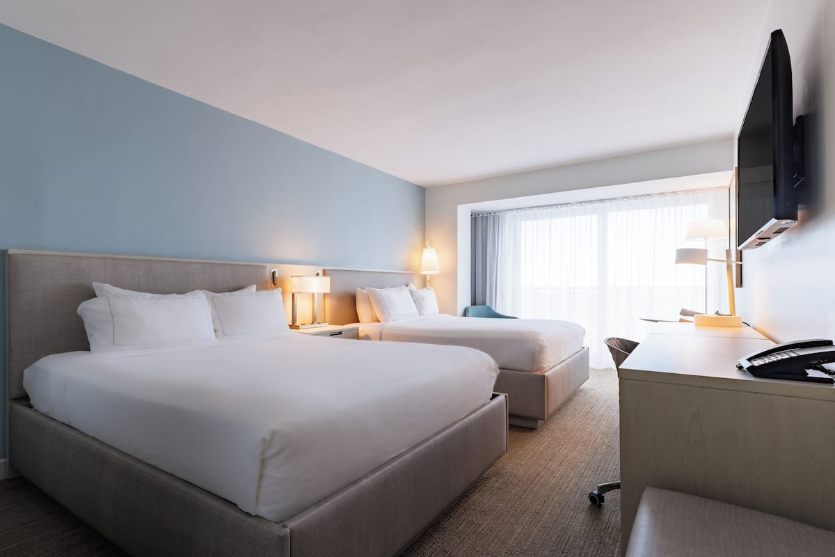 A hotel room with two beds, a desk, a TV, and a window with curtains.