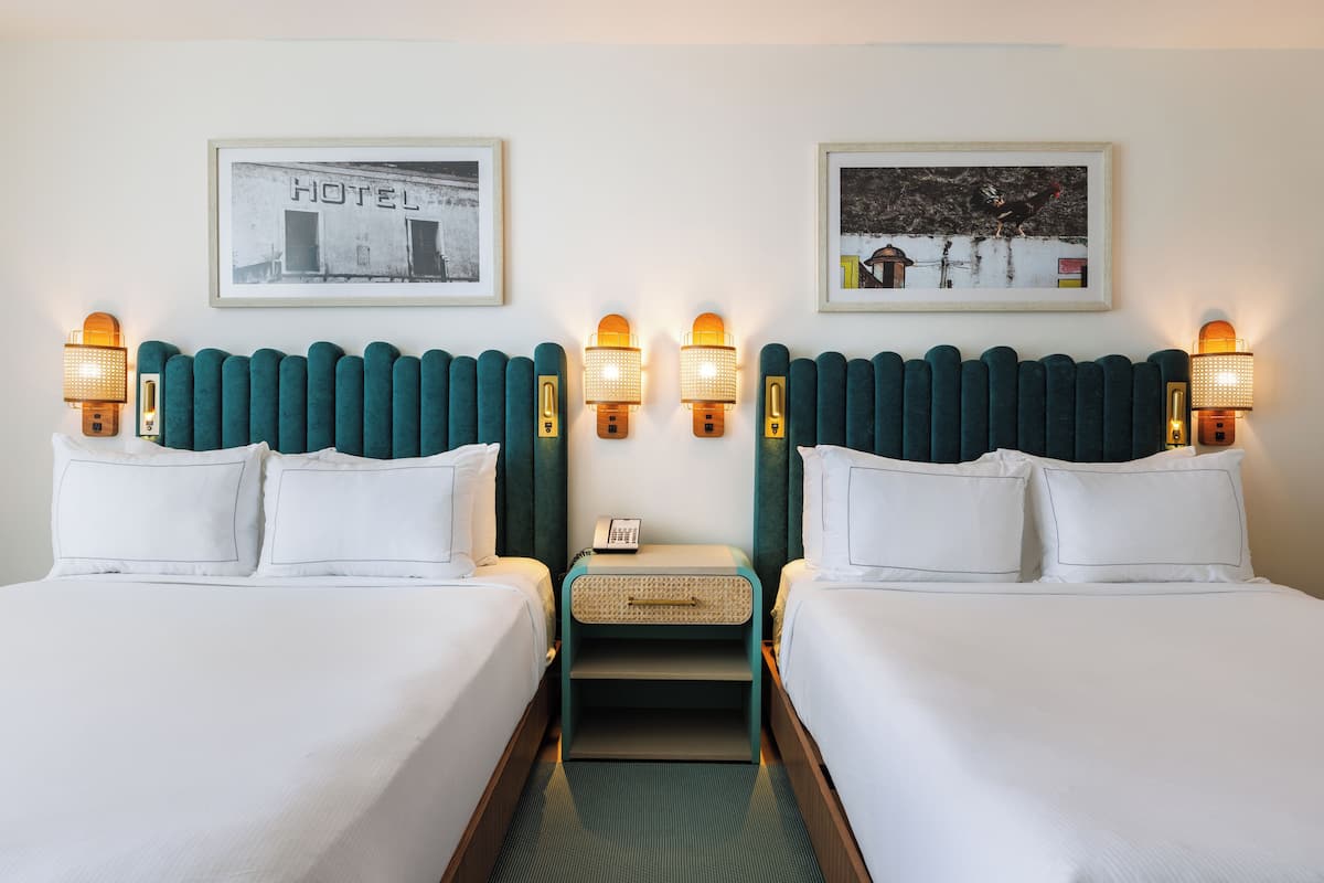A hotel room with two beds, a nightstand, and wall-mounted lamps.