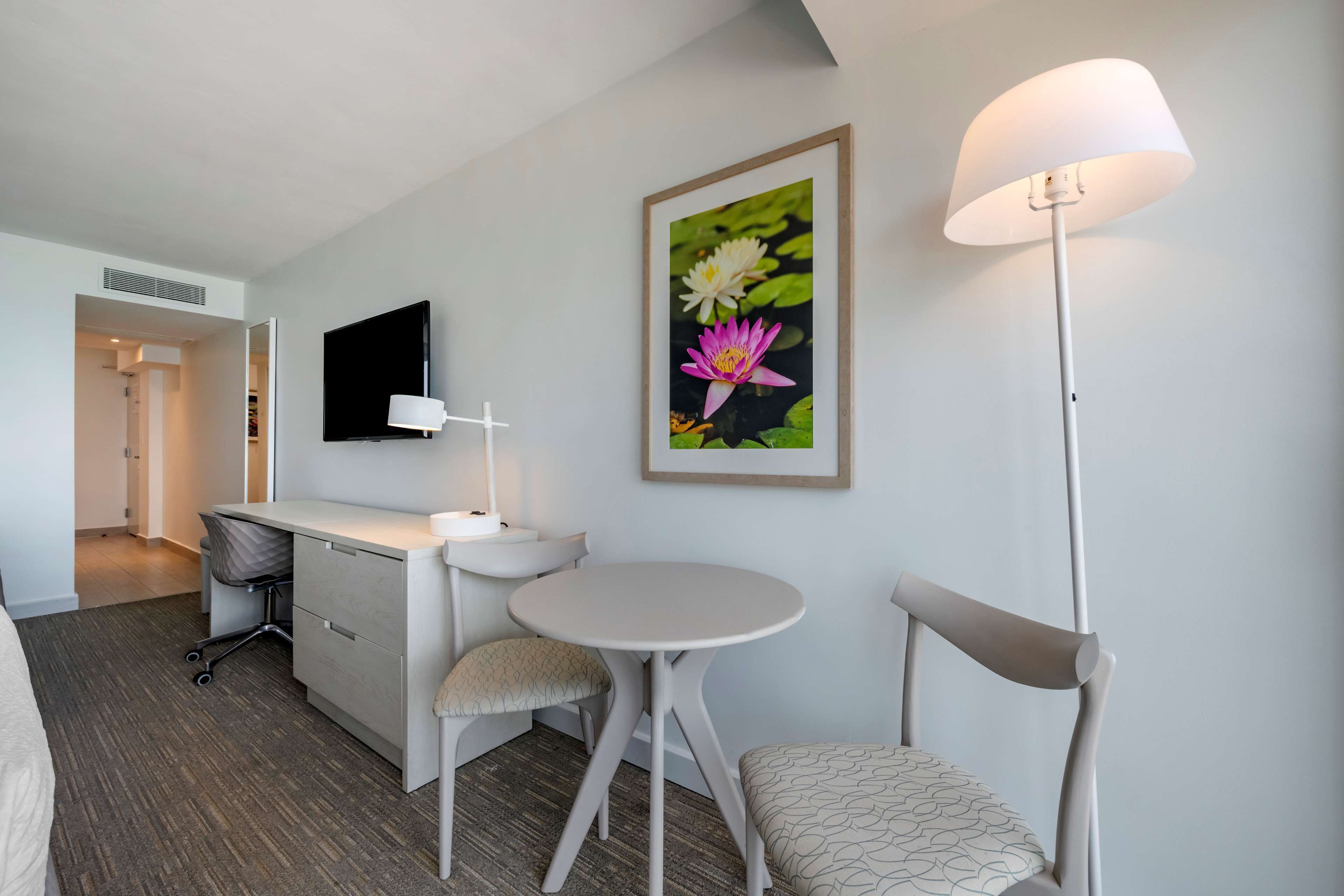 A hotel room with a desk, chair, round table, and a standing lamp.