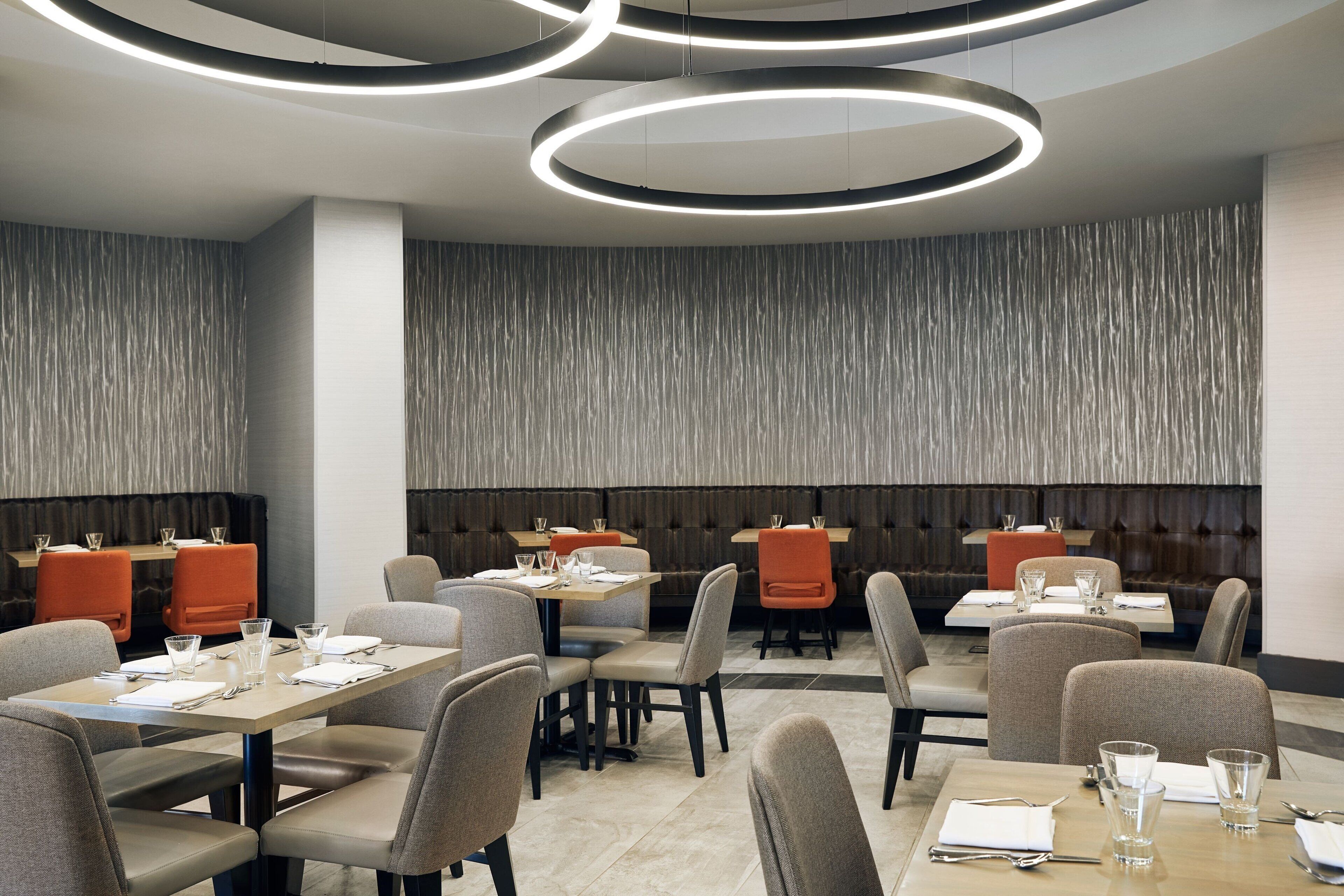 A modern dining area with circular ceiling lights, grey upholstered chairs, and a textured wall.