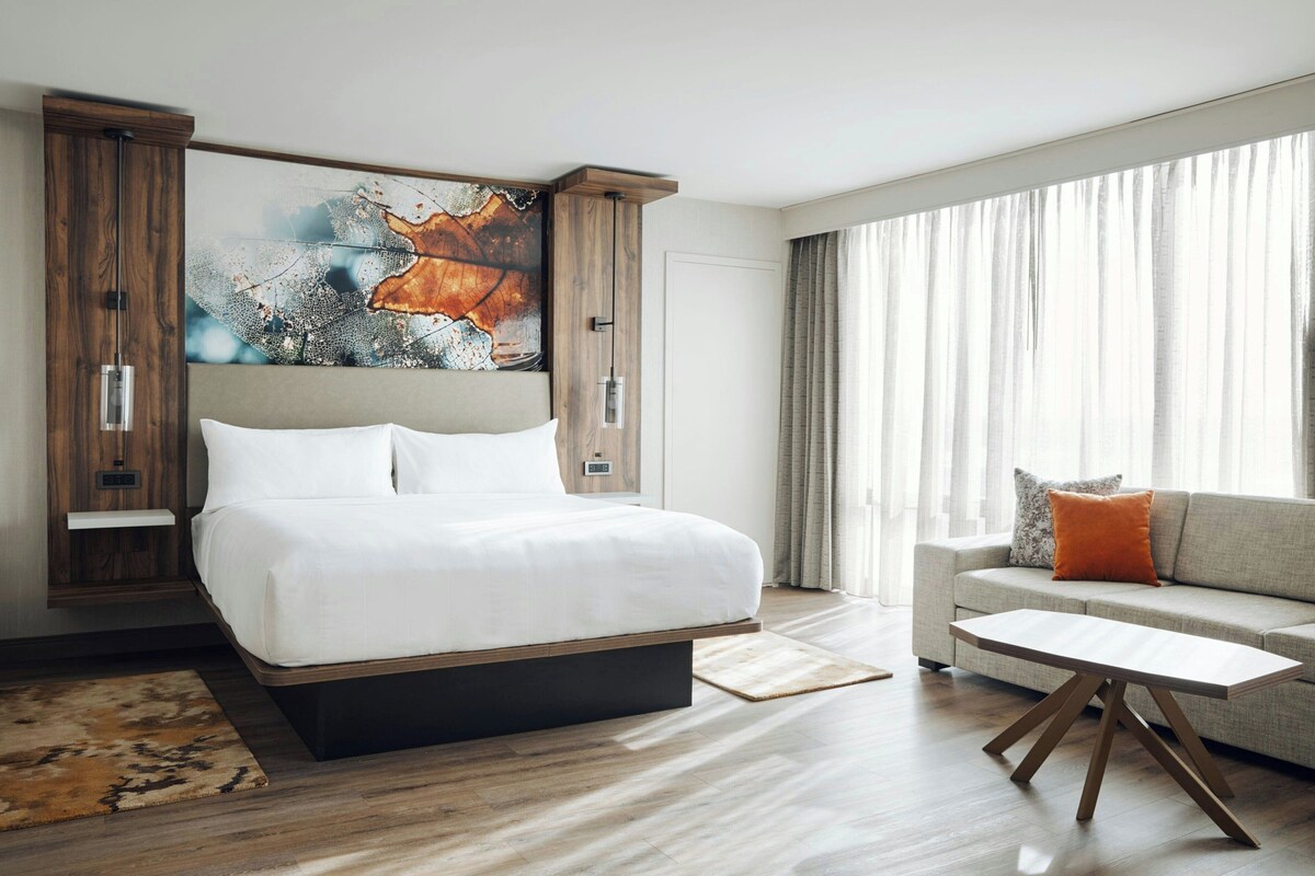 Habitación de hotel moderna con una cama grande, un sofá, una mesita de café y un cuadro abstracto de gran tamaño en la pared.