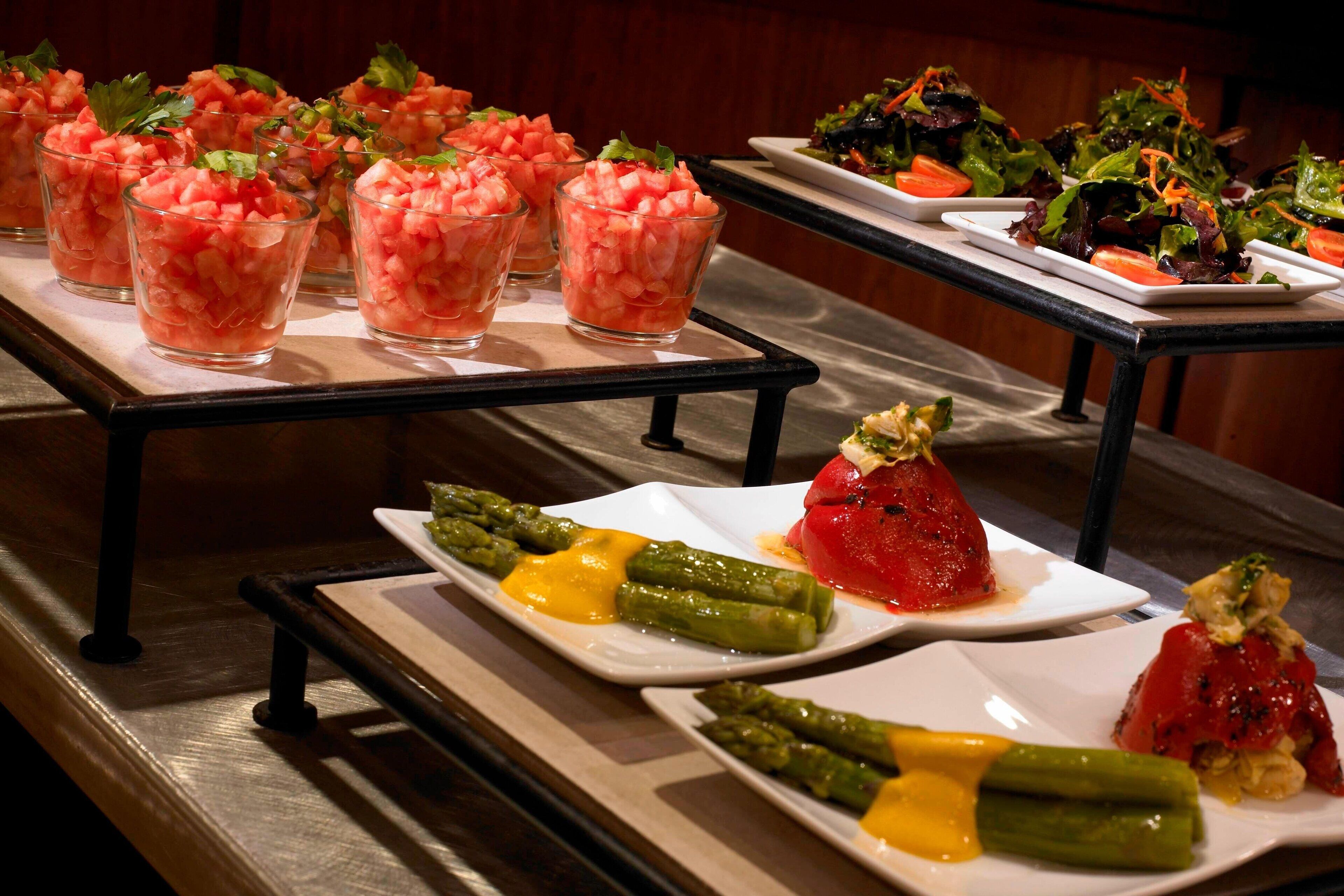 A buffet with various dishes including watermelon salad, asparagus with cheese, and stuffed tomatoes.