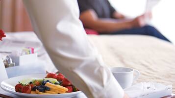 A breakfast tray with fruits and a cup on a bed.