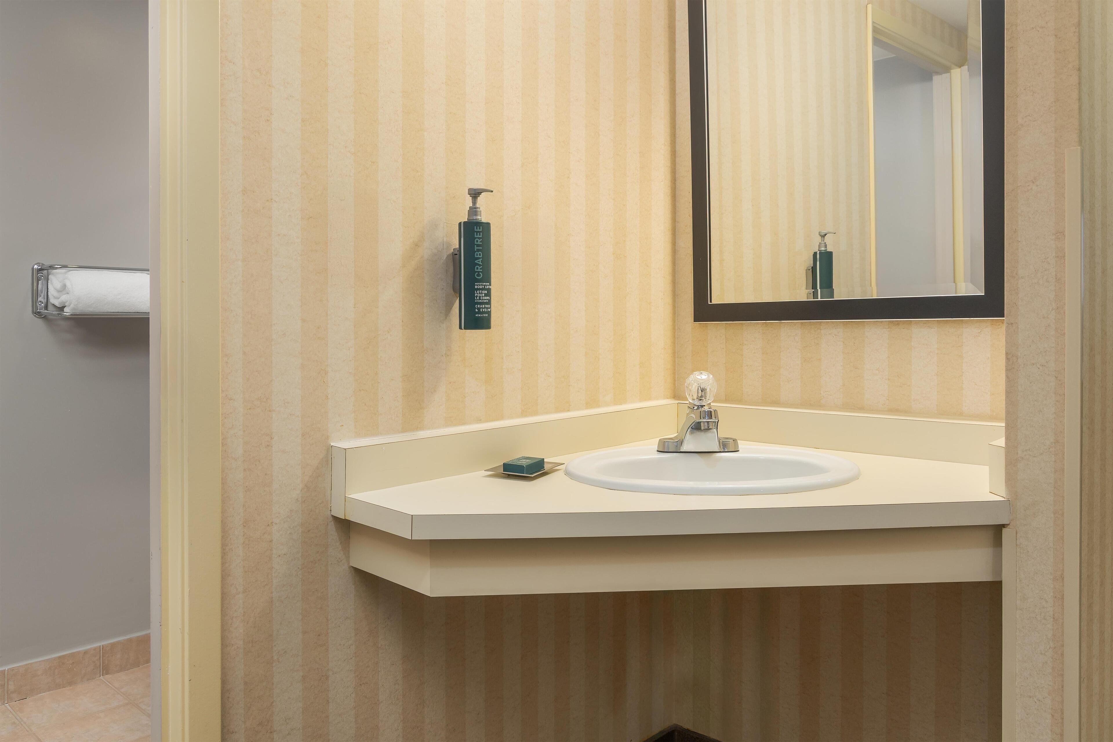 A bathroom with a striped wallpaper, a white sink, a mirror, and a hand soap dispenser.