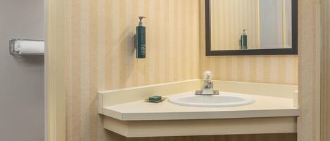 A bathroom with a striped wallpaper, a white sink, a mirror, and a hand soap dispenser.