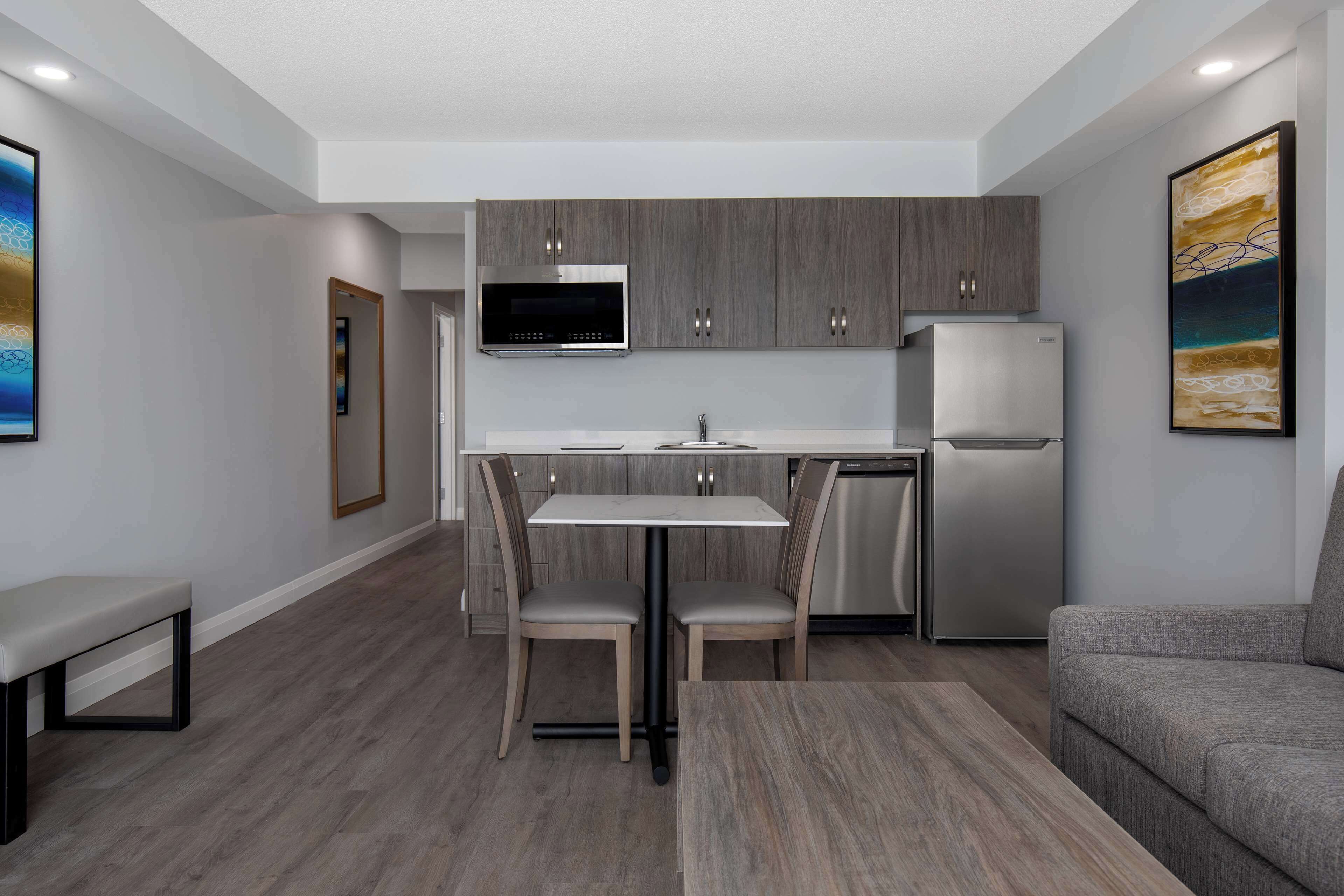 Una cocina moderna con gabinetes grises, un refrigerador de acero inoxidable y un microondas empotrado. Hay una mesa de comedor con dos sillas y un banco.