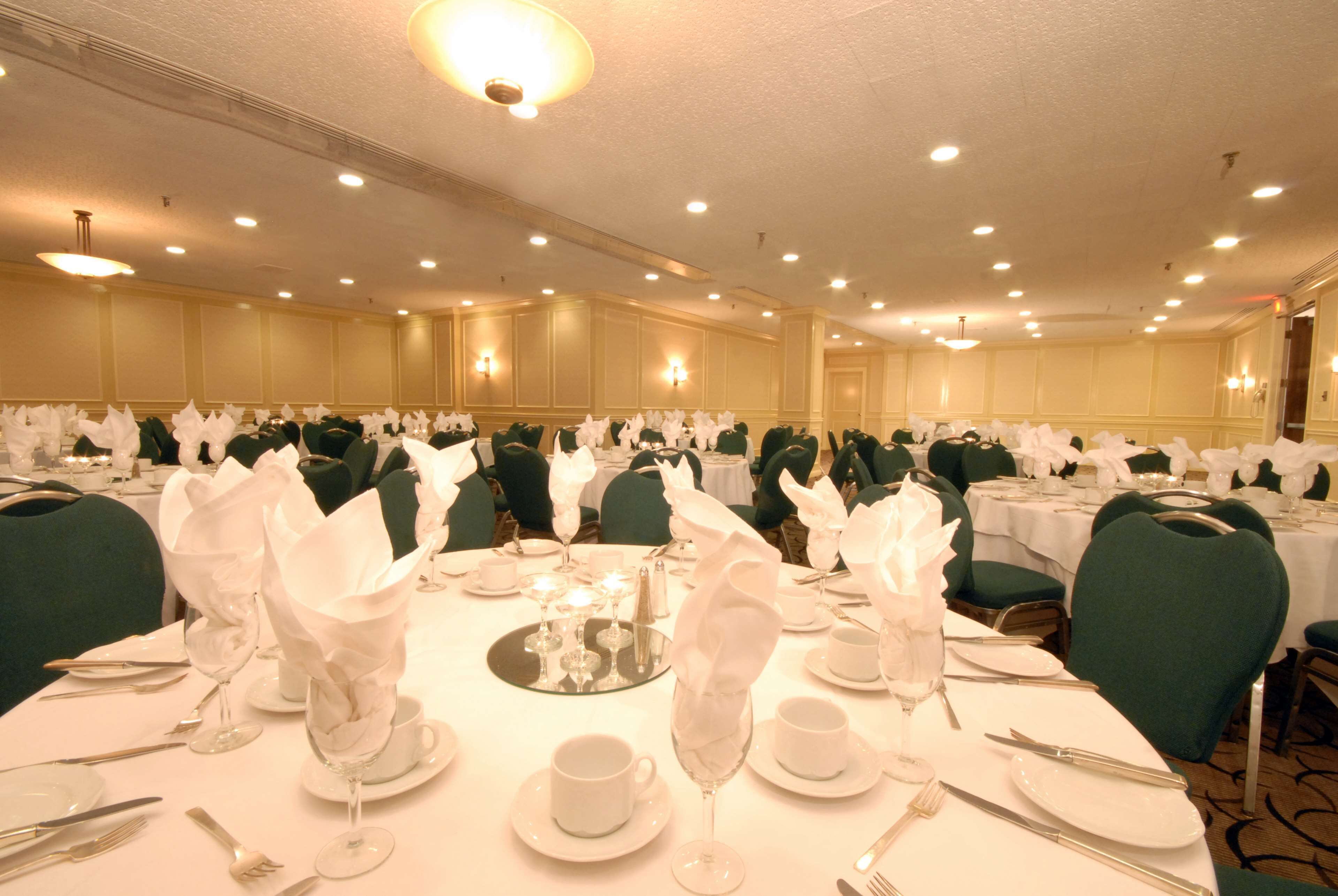 A banquet hall with round tables set for dining, each with white napkins, plates, and cutlery.
