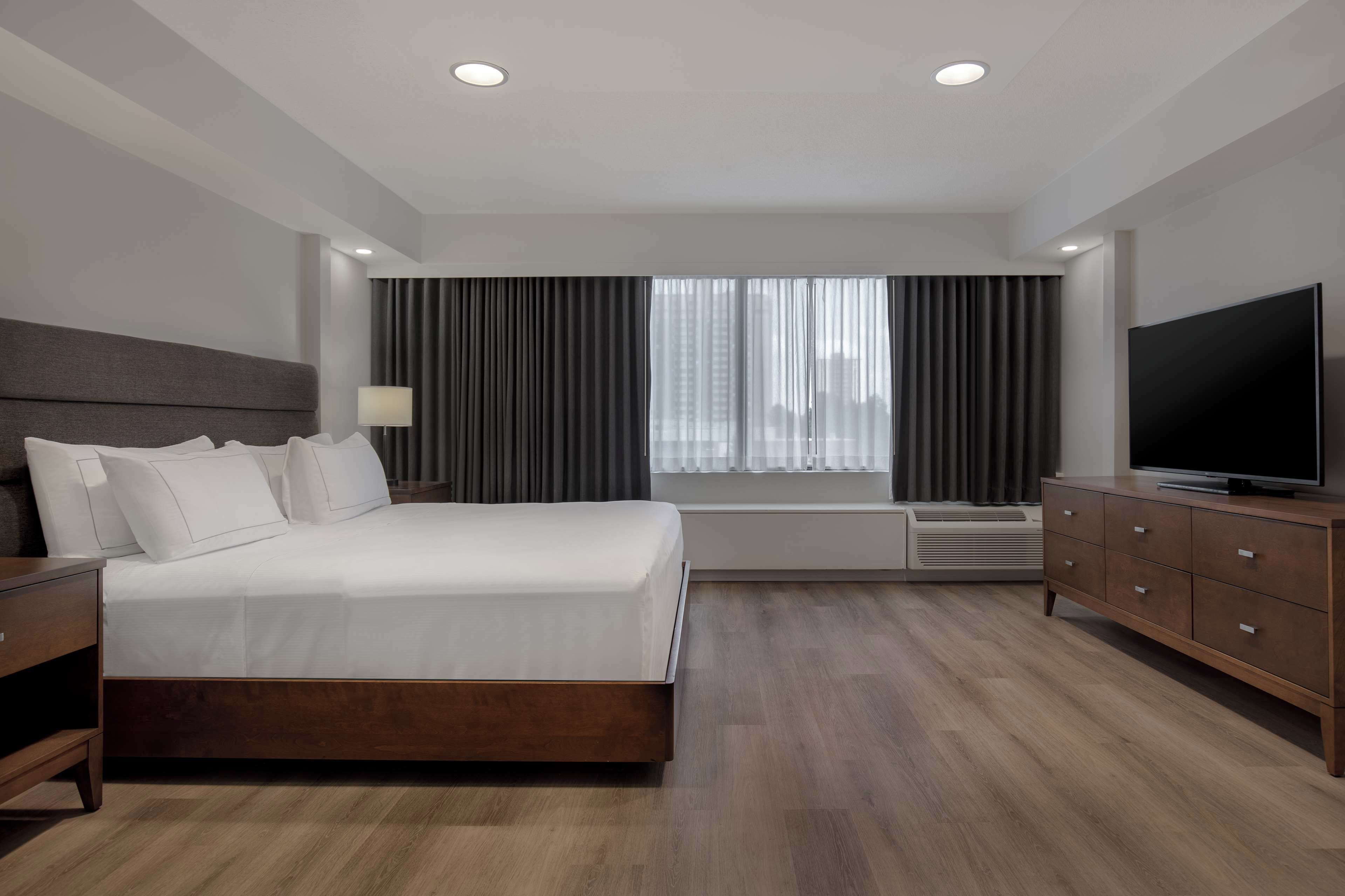 A modern hotel room with a large bed, a TV, a dresser, and a window with curtains.