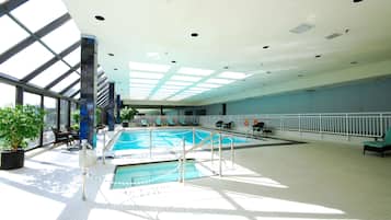 An indoor swimming pool with a glass ceiling, surrounded by lounge chairs and potted plants.