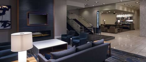 Un vestíbulo moderno con una zona de estar, una escalera y una estación de café Starbucks.