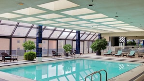 An indoor swimming pool with clear glass walls, lounge chairs, and potted plants. - DoubleTree by Hilton Hotel London Ontario (London)