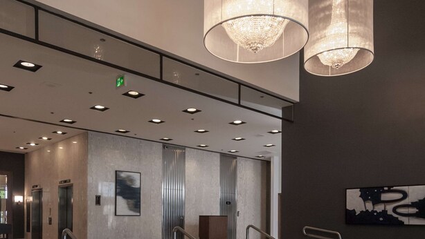 A modern hotel lobby with large, cylindrical chandeliers, a staircase with metal railings, and a patterned carpet. - DoubleTree by Hilton Hotel London Ontario (London)