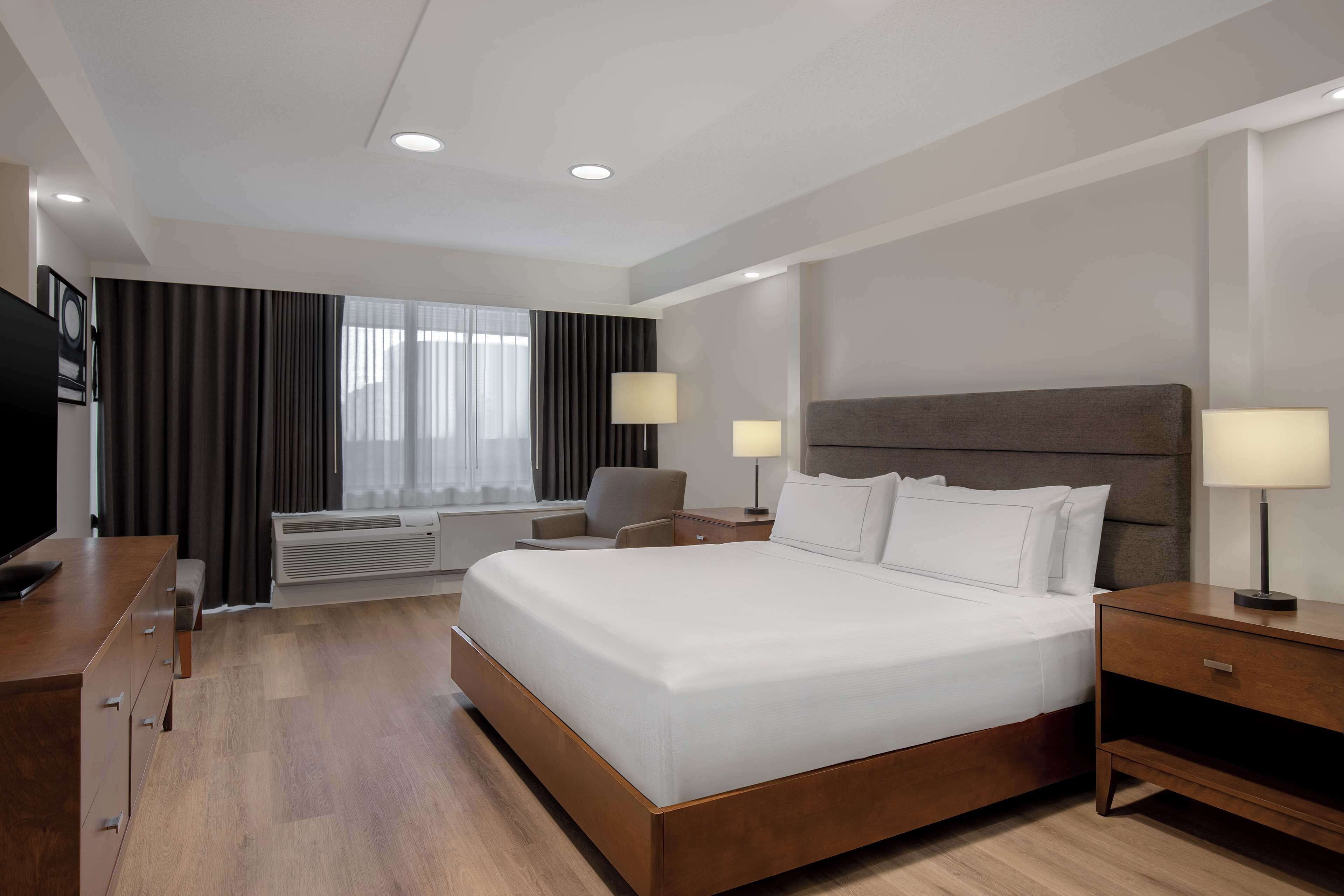 Una habitación de hotel moderna con una cama grande, mesitas de noche, un escritorio y un televisor.