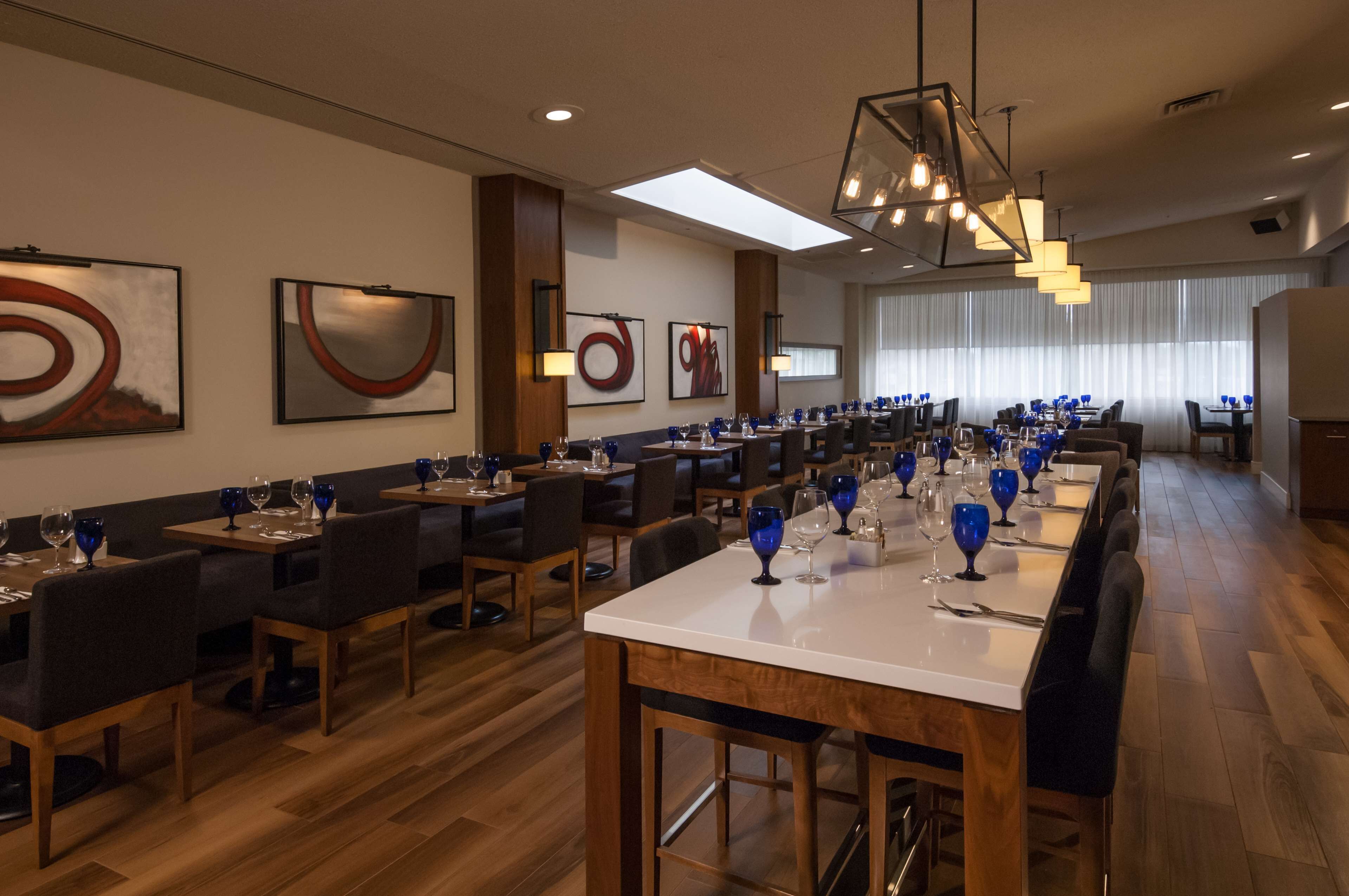 Un restaurant doté de nombreuses tables, chacune agrémentée de verres à vin et d’assiettes bleues, et présentant un aménagement intérieur moderne avec des œuvres d’art abstraites sur les murs.