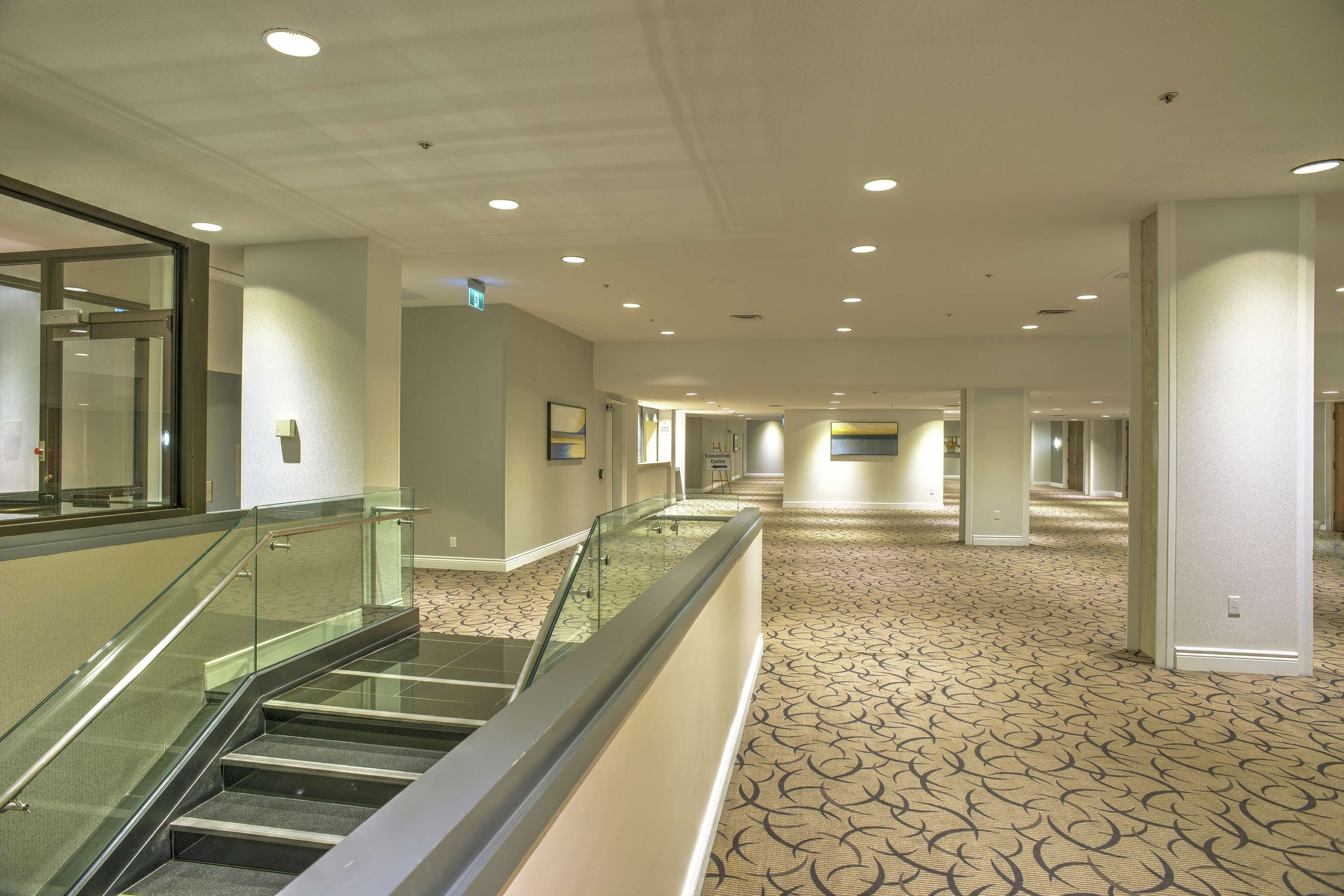 A hotel corridor with a carpeted floor, glass railings, and recessed lighting.