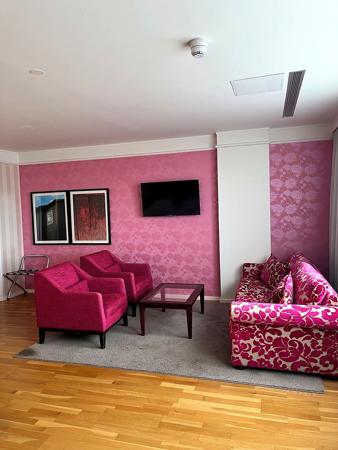 Una sala de estar con una pared rosa, un televisor de pantalla plana, dos sillones, una mesa de centro y un sofá estampado.