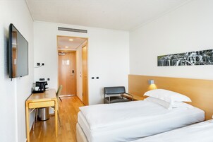 Habitación de hotel con cama, escritorio con cafetera, una silla, televisor montado en la pared y un cuadro de una cascada.