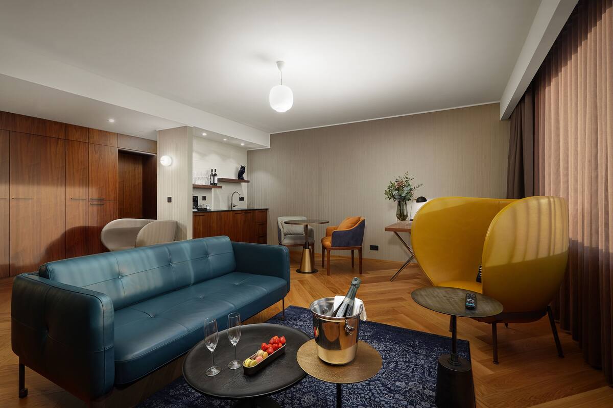 Un salon moderne avec un canapé bleu, un fauteuil jaune, un coin repas avec une table et des chaises, et une cuisine en arrière-plan.