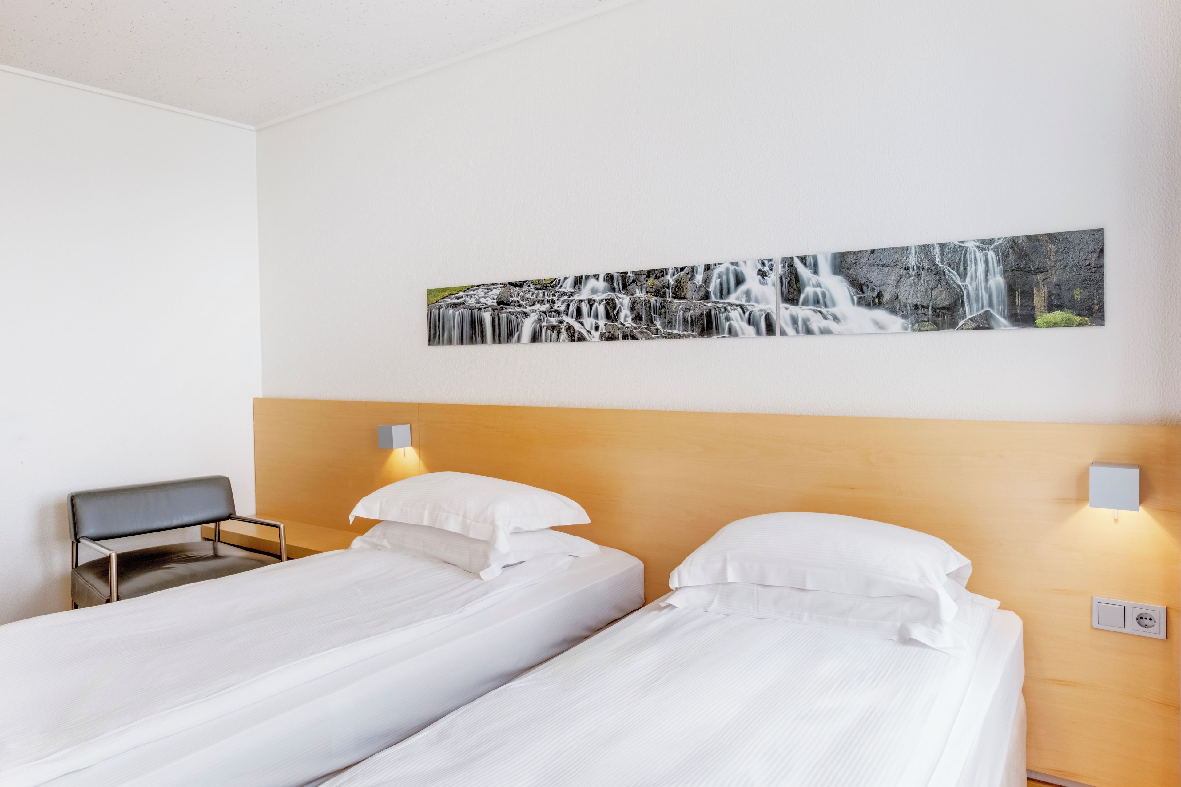 A hotel room with two single beds, a wooden headboard, a desk, and a wall-mounted picture of a waterfall.