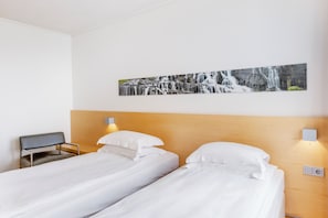 Habitación de hotel con dos camas individuales, un cabecero de madera, un escritorio y un cuadro de una cascada colgado en la pared.