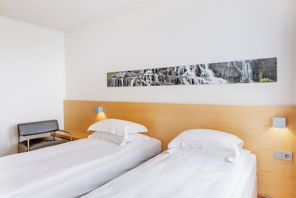 A hotel room with two single beds, a wooden headboard, a desk, and a wall-mounted picture of a waterfall.