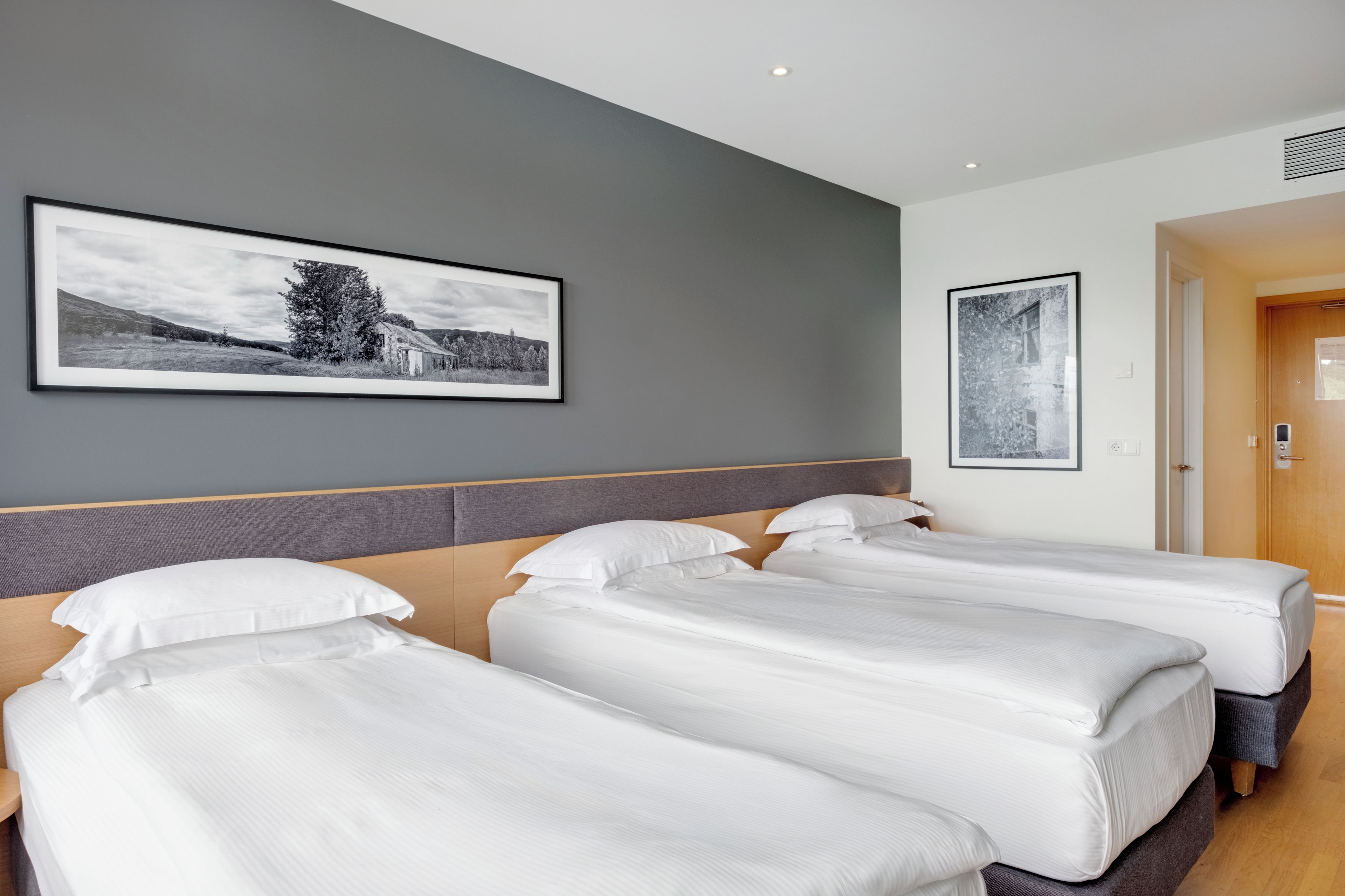 Een hotelkamer met twee enkele bedden, een grijze hoofdbord en twee zwart-wit foto’s in lijsten aan de muur.