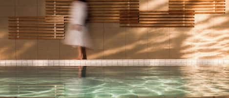 En person står vid en pool med ett kaklat golv och en vägg med horisontella träribbor.