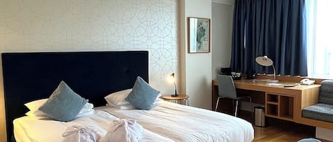 A hotel room with a large bed, a desk, and a chair.