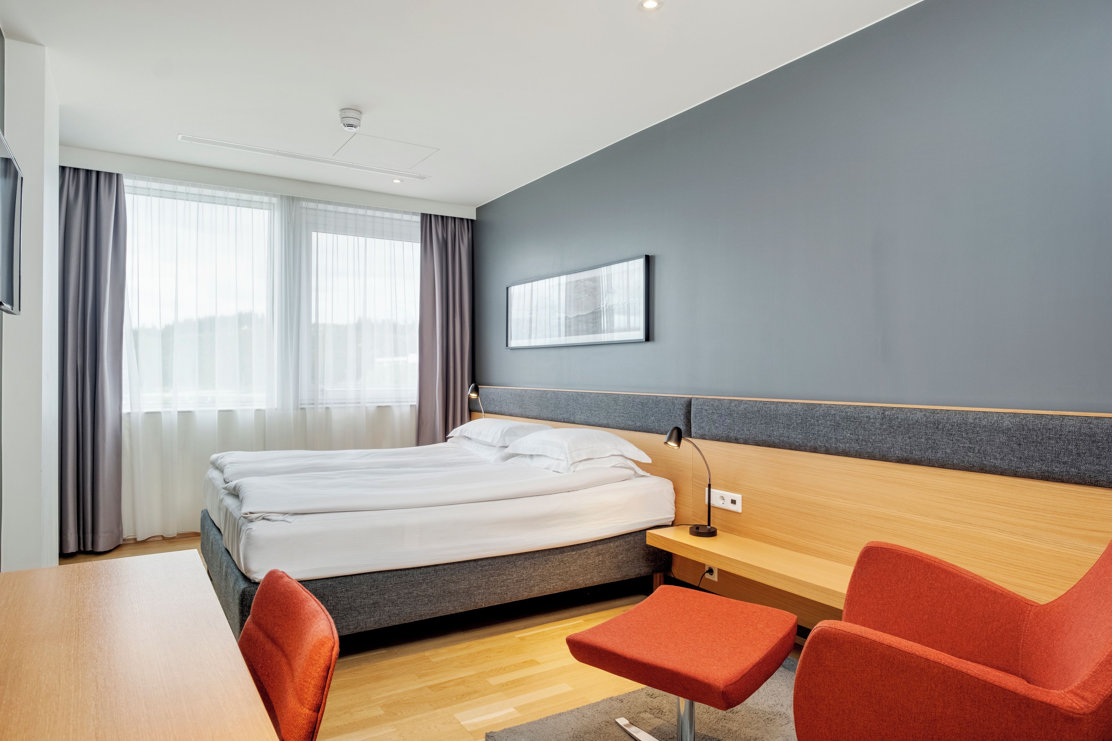 A modern hotel room with a bed, a desk, and a chair.