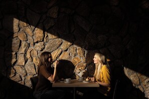 Deux personnes sont assises à une table, avec un mur de pierres en arrière-plan.