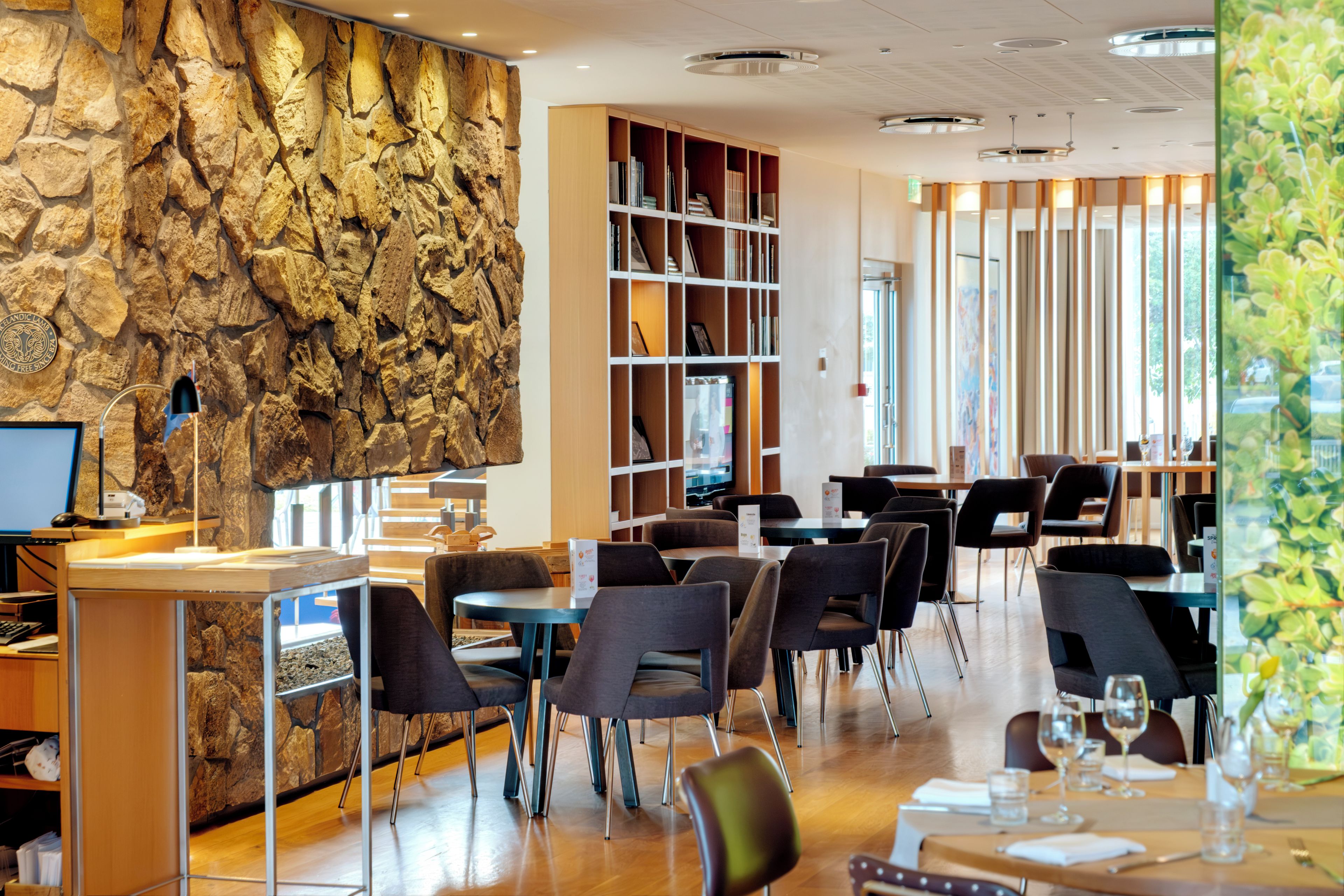 A modern restaurant interior with a stone wall, wooden bookshelves, and a variety of seating arrangements.