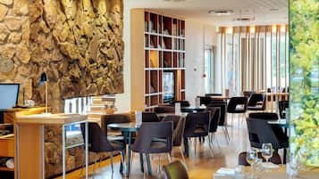 A modern restaurant interior with a stone wall, wooden bookshelves, and a variety of seating arrangements.