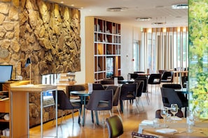 A modern restaurant interior with a stone wall, wooden bookshelves, and a variety of seating arrangements.
