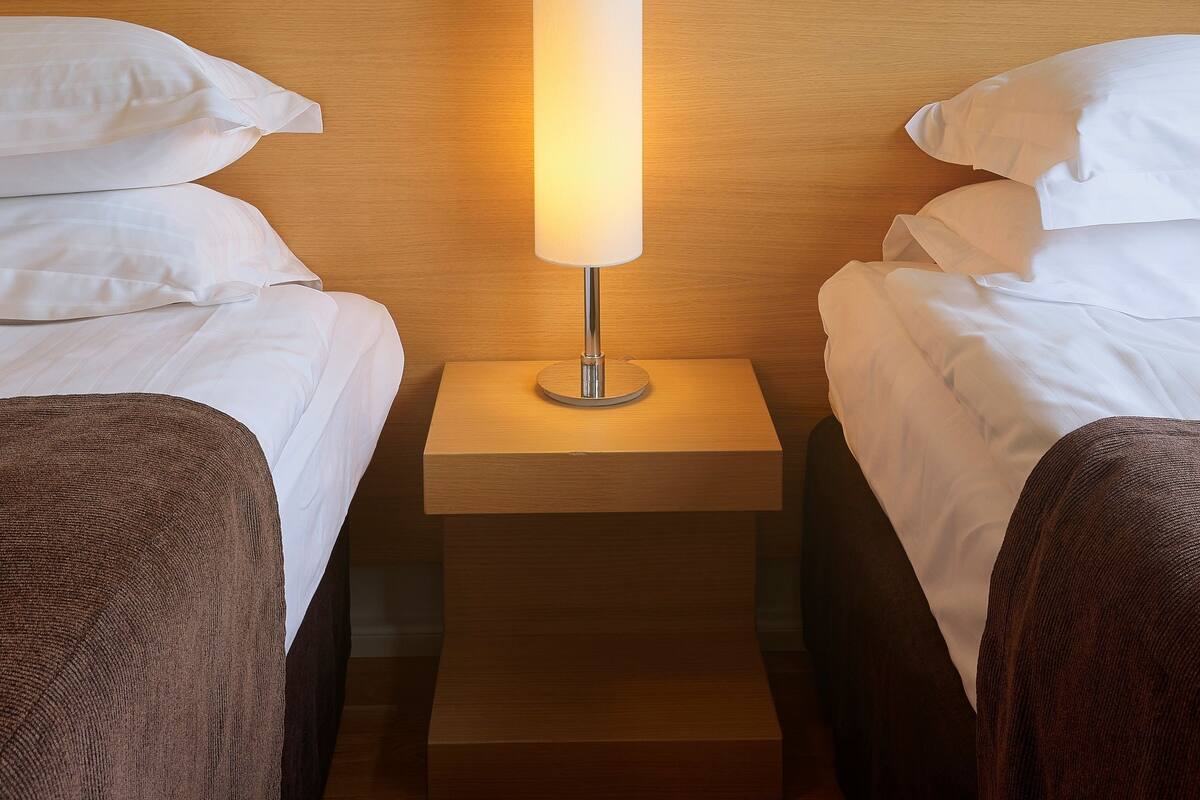 Une chambre d’hôtel avec deux lits, une tête de lit en bois, une table de chevet avec une lampe et une petite table de nuit.