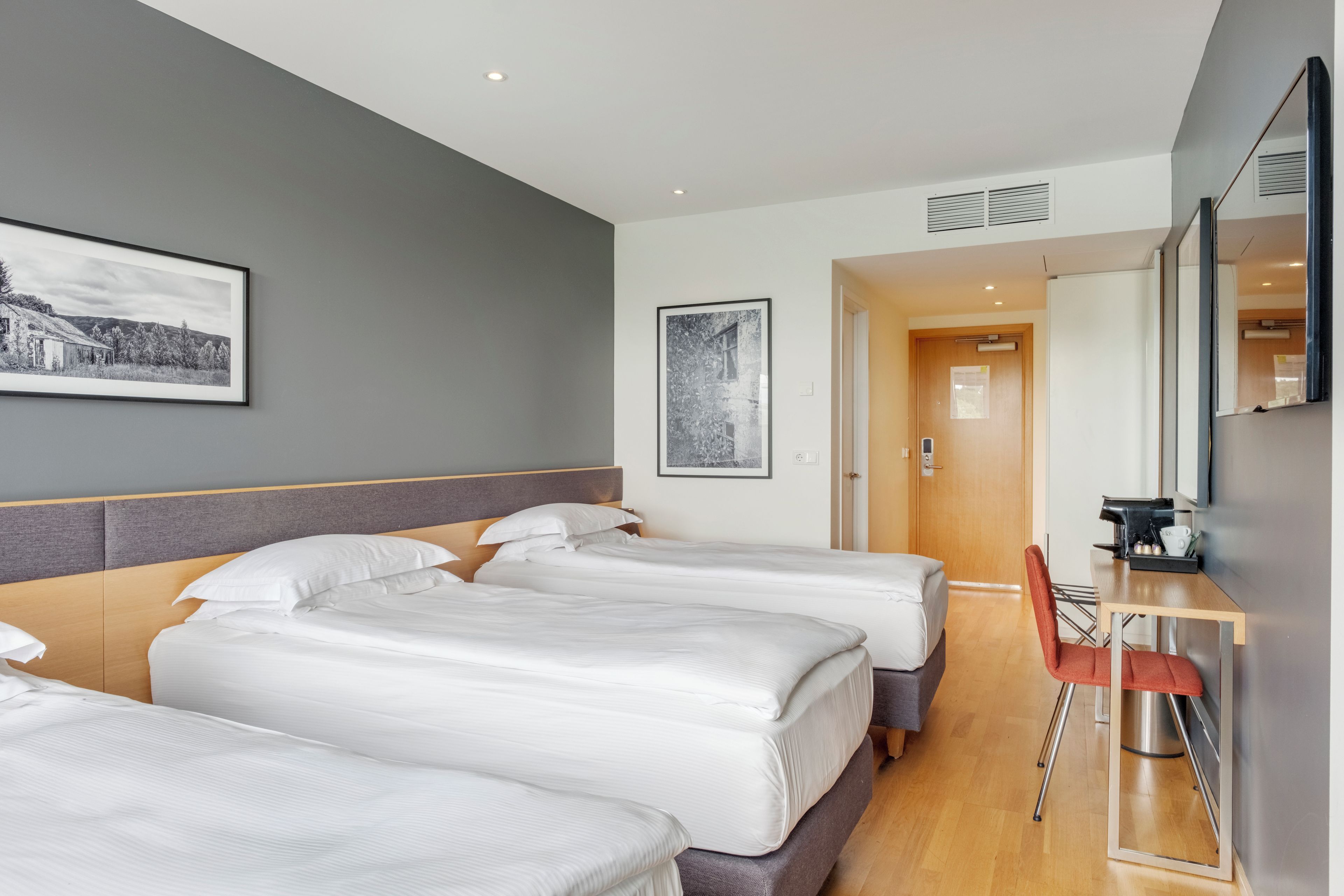 A hotel room with three beds, a desk, and a mirror.