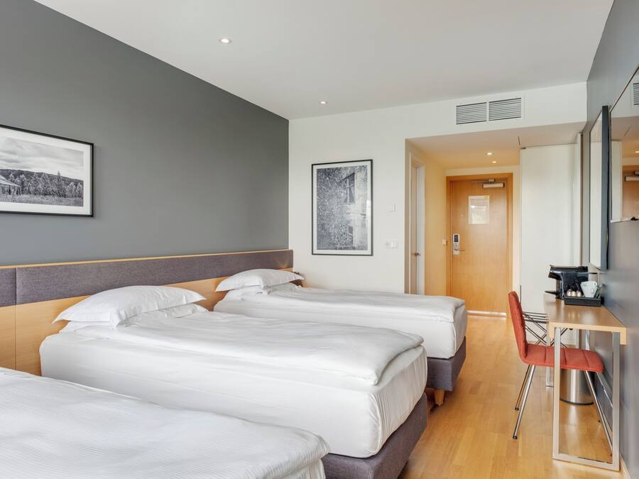 A hotel room with three beds, a desk, and a mirror.