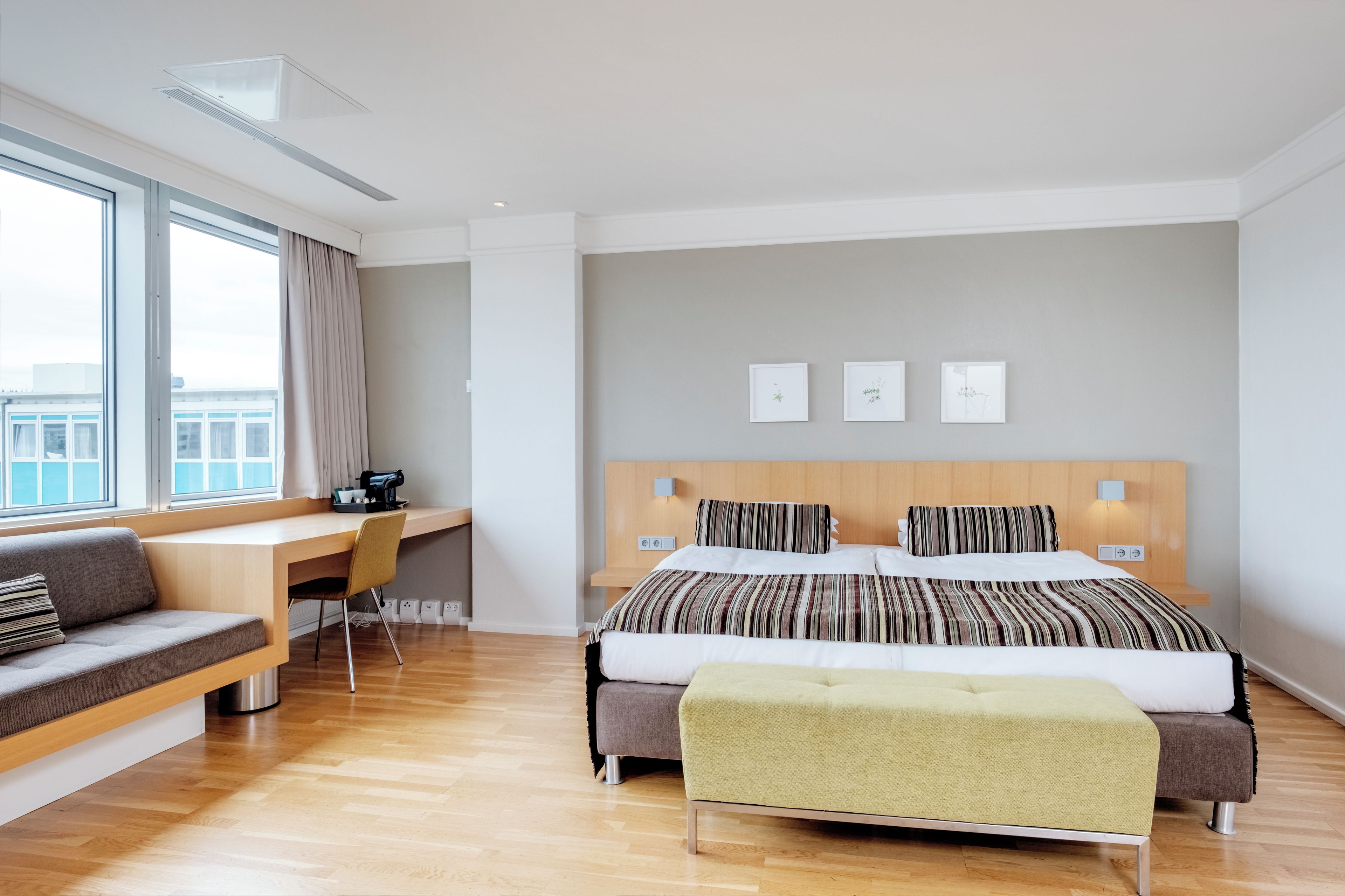A modern hotel room with a large bed, a desk, and a sofa.