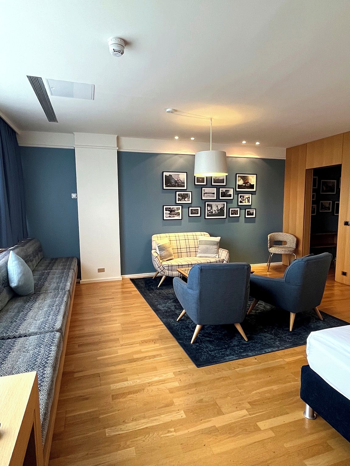 Una sala de estar moderna con un sofá, dos sillones, una mesa de centro, un tapete y una pared con cuadros.