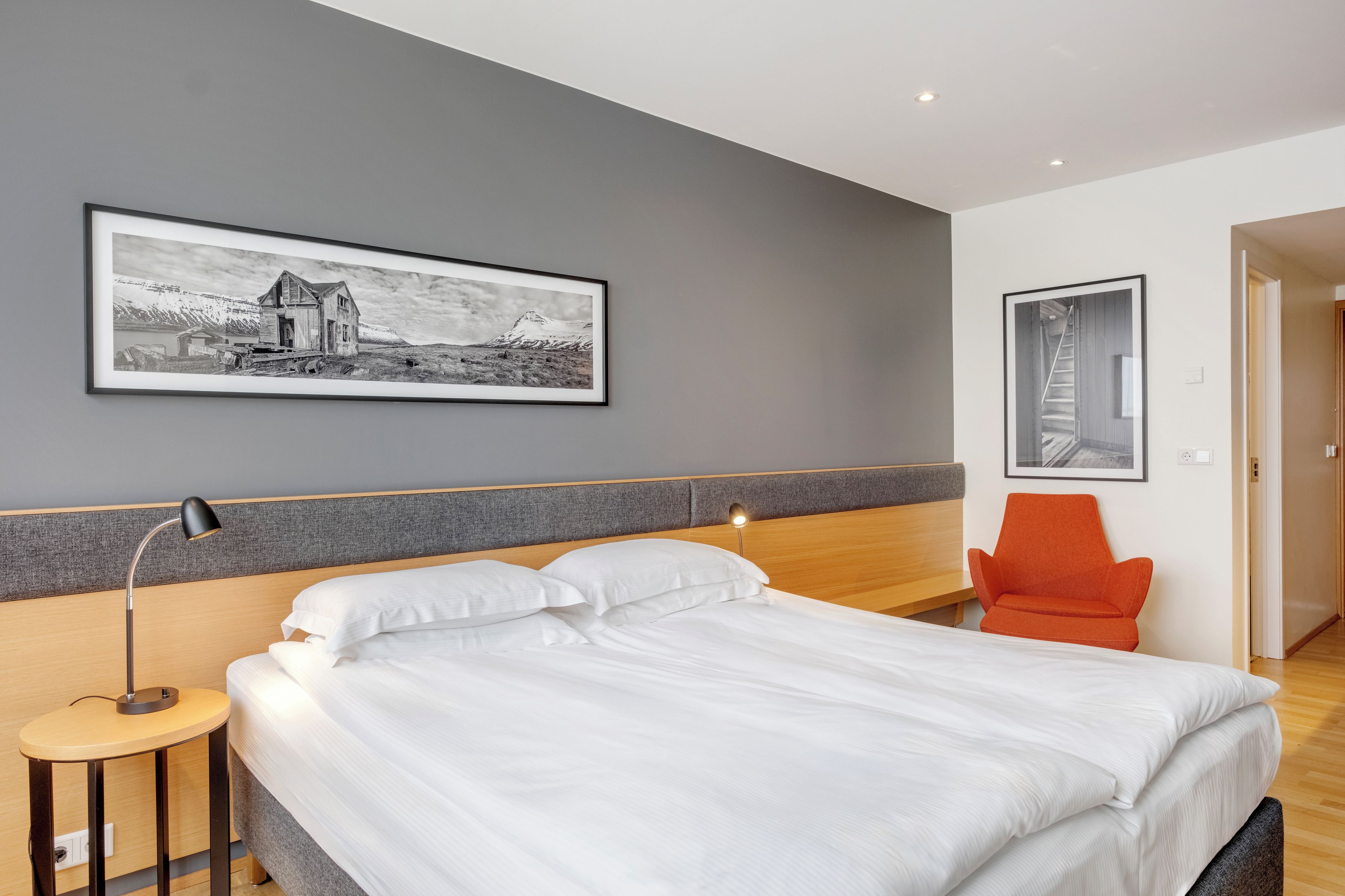 Een moderne hotelkamer met een groot bed, een bureau, een stoel en twee ingelijste foto's aan de muur.