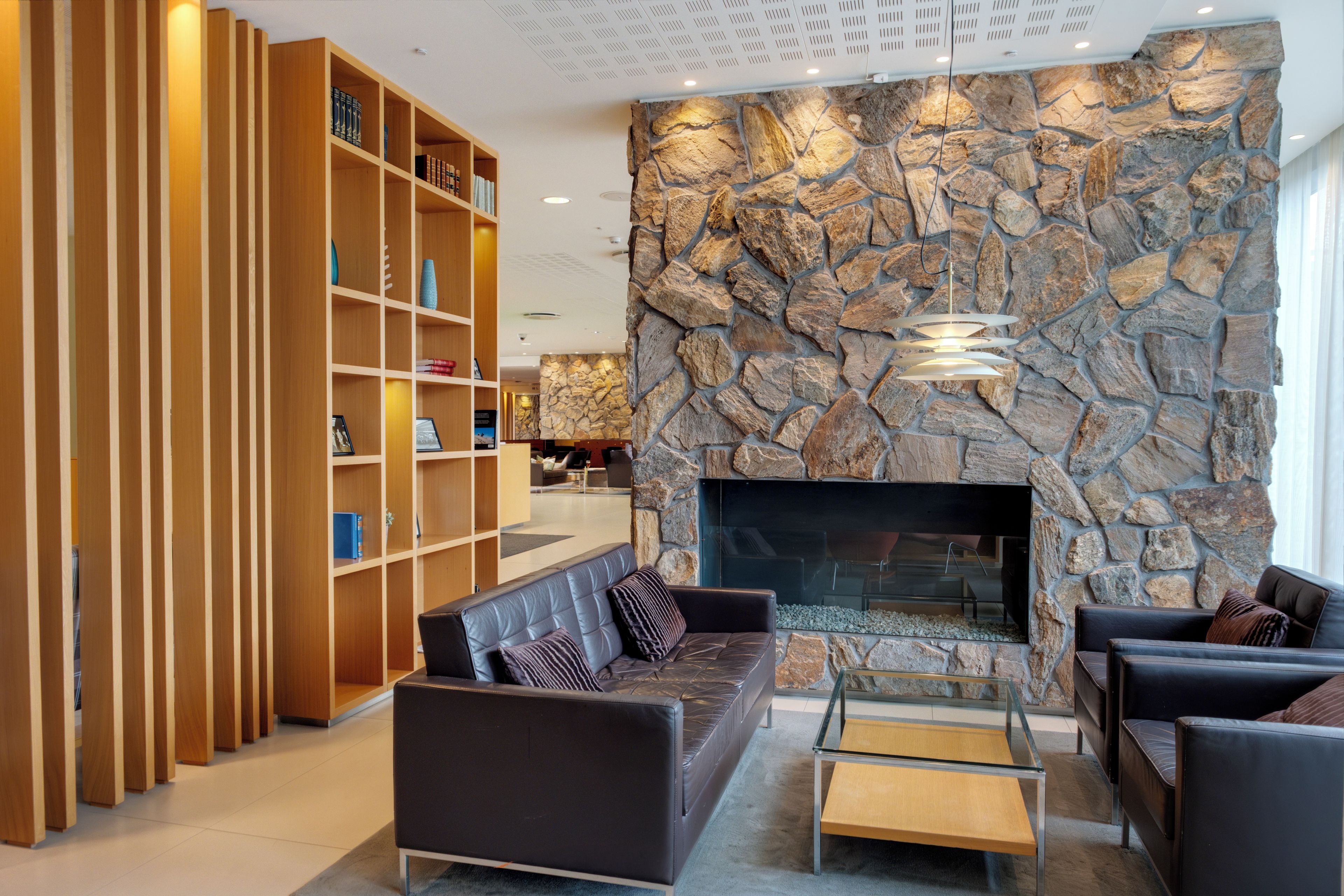 Uma sala de estar moderna com parede de pedra, lareira e um conjunto de sofás.
