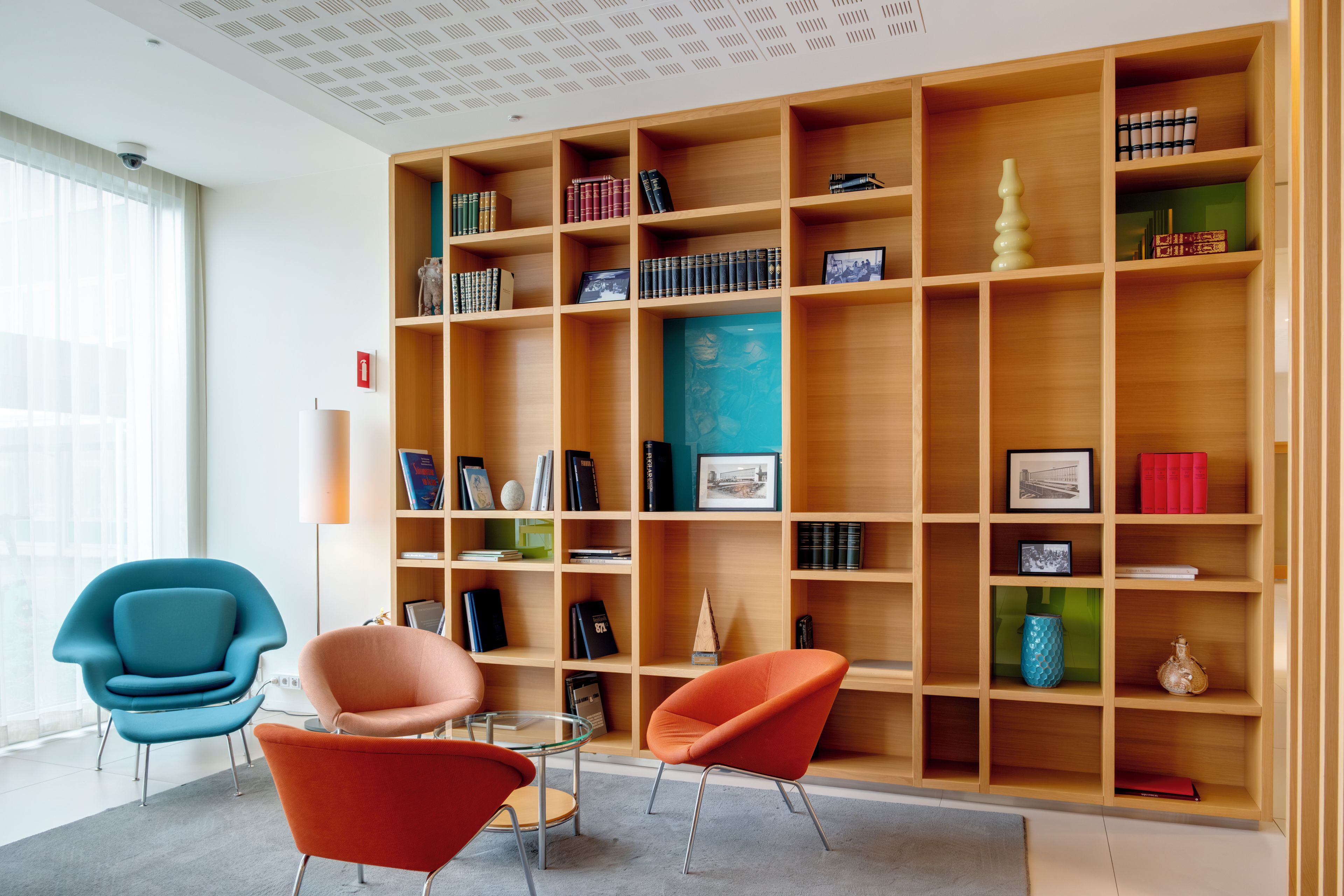 A modern library with wooden bookshelves, a glass table, and two chairs.
