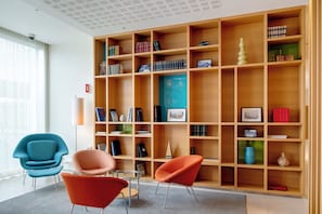 A modern library with wooden bookshelves, a glass table, and two chairs. - Hotel Reykjavik Askja (Reykjavik)