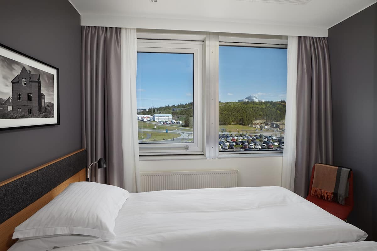 Une chambre d’hôtel avec un grand lit, une vue sur un parking et des immeubles, et un tableau encadré au mur.