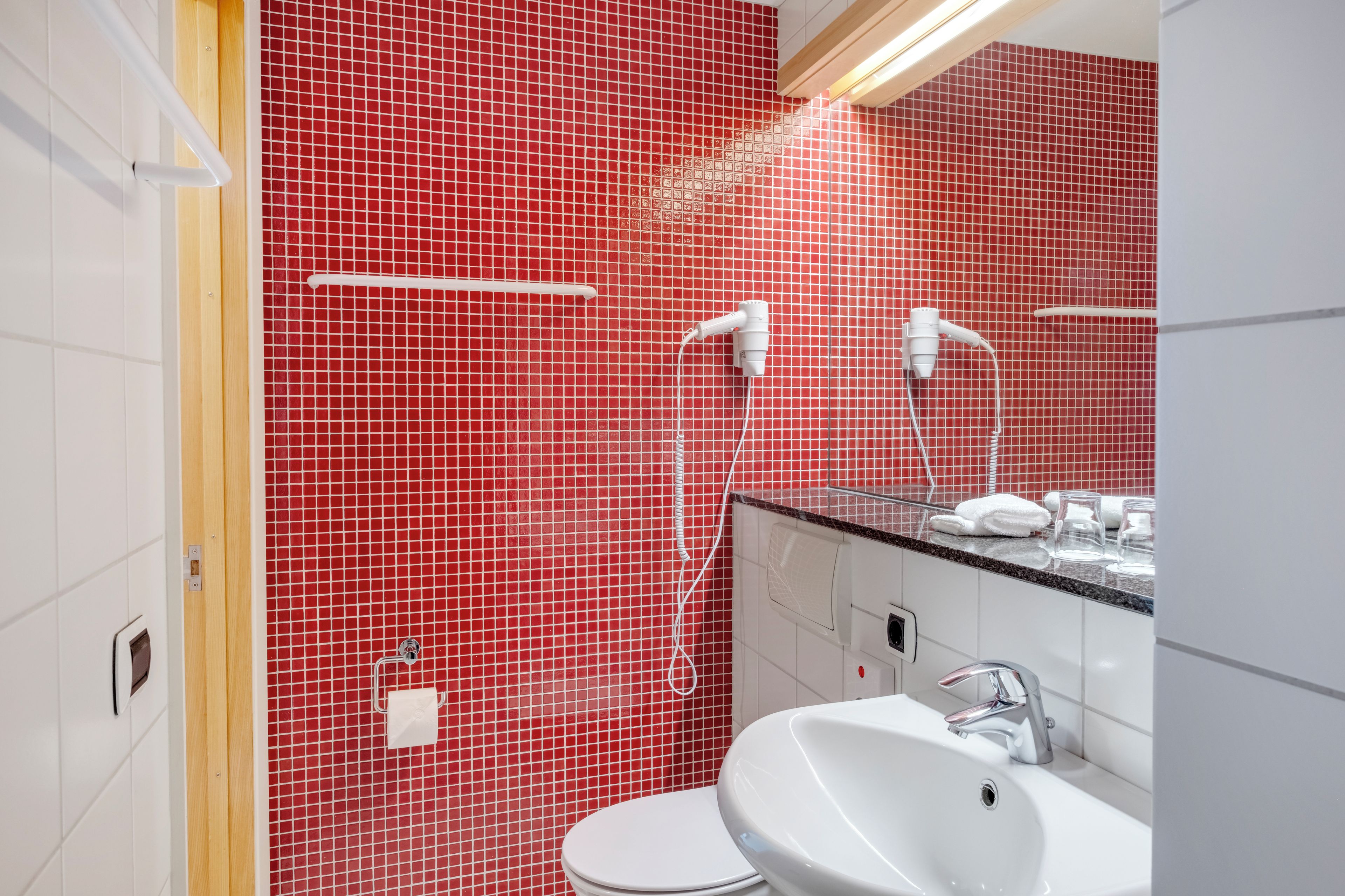A bathroom with a red tiled wall, a white sink, a mirror, and a shower.
