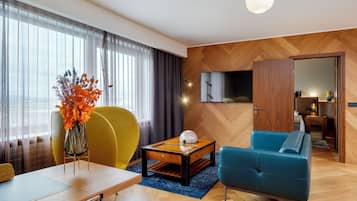 A modern living room with a wooden herringbone floor, a blue sofa, a yellow armchair, a wooden coffee table, and a glass vase with orange leaves.