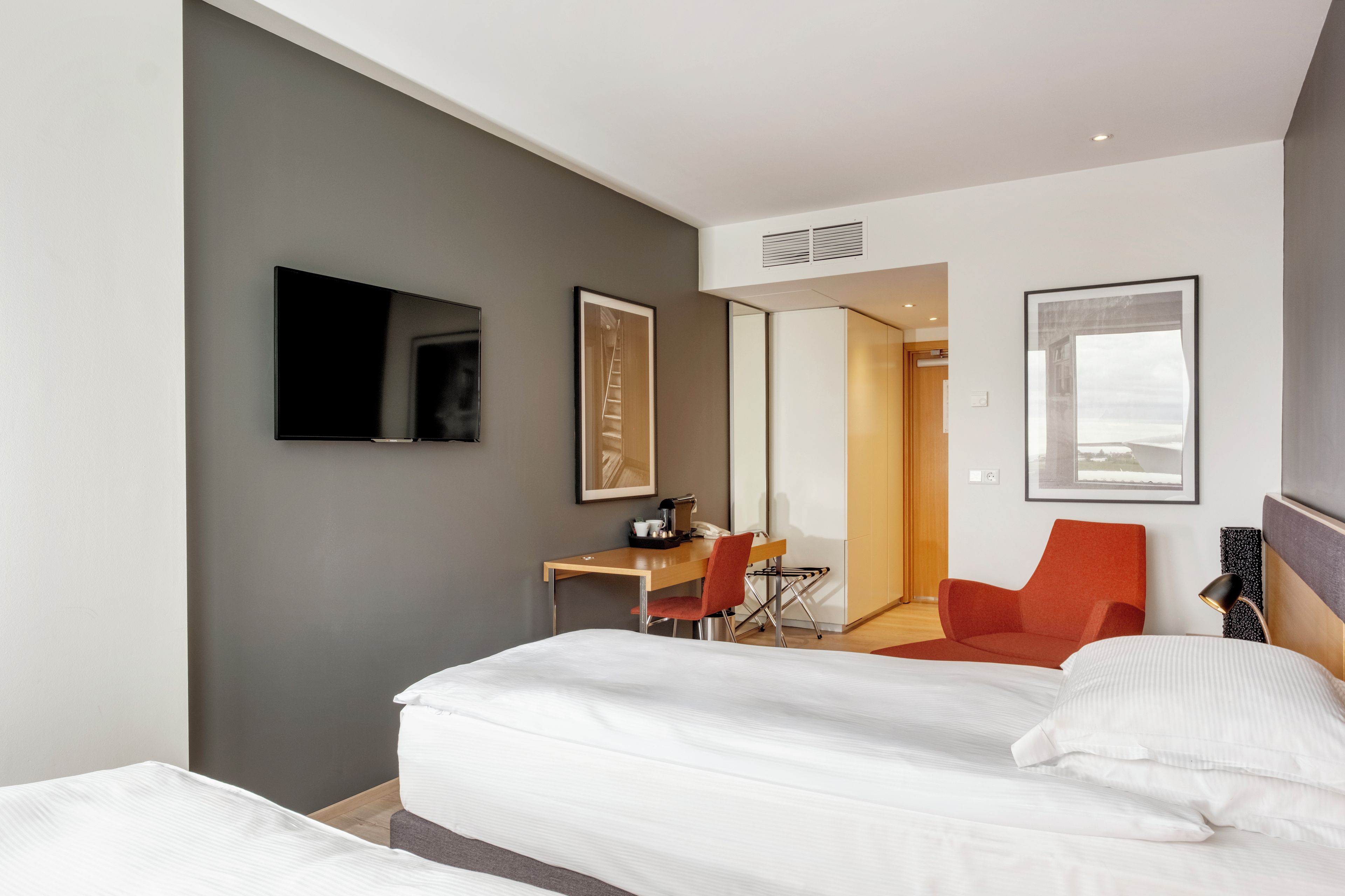 A modern hotel room with a bed, a desk, a chair, and a television.